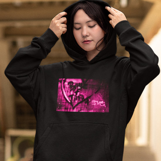 A female model wearing a black hoodie sweatshirt. On the front of the hoodie is a pink and black spraypaint design with a heart that says "Better & Tine 4 Ever."  Behind the model is a blurred hallway.