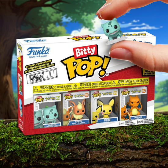 A cardboard package containing 4 minature Pokemon Funkp Pop figurines. The four figurines are at the bottom in a row, including Bulbasaur, Flareon, Pichu, and Charizard. The package is on a mossy tree limb, with a forest in the background. In front of the package is a model's hand holding a miniature Bulbasur.