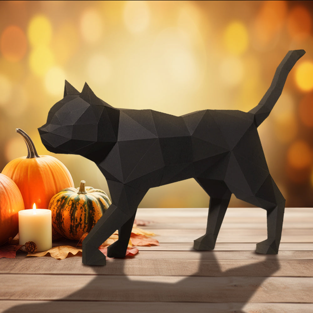 A paper model of a black cat standing on a wooden table, next to a collection of small pumpkins and a candle. In the background is a field of orand and yellow lights.