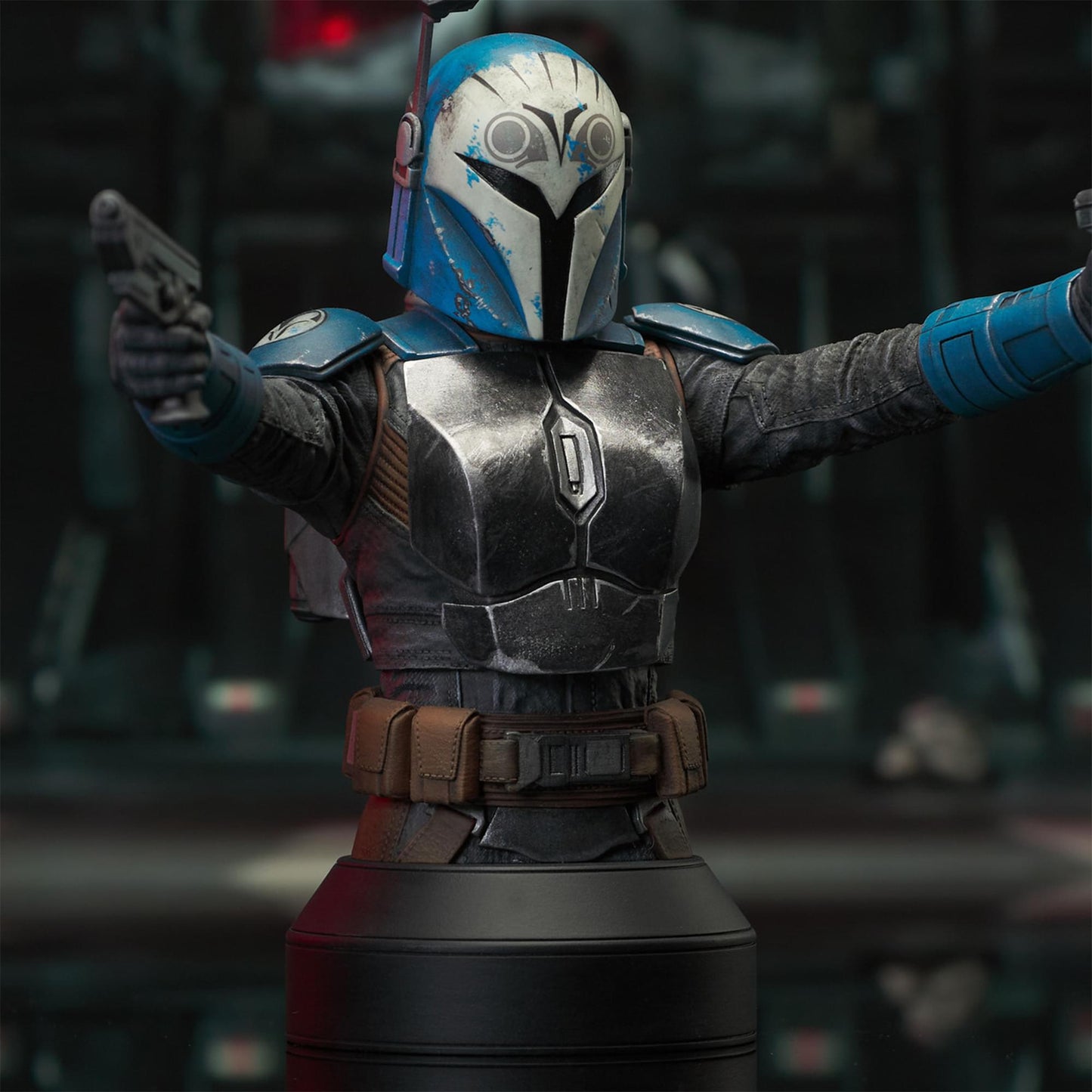 A resin bust depicting Bo-Katan Kryze in her Nite Owl armor, holding blasters in each outstretched hand. In the background is a hangar bay.