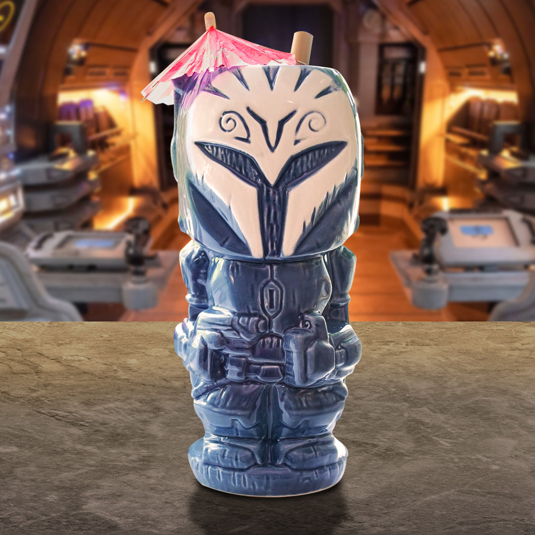 A blue tiki mug depicting the Mandalorian character Bo Katan. A pink umbrella is in the top of the mug. In the background is the bridge of a spaceship.