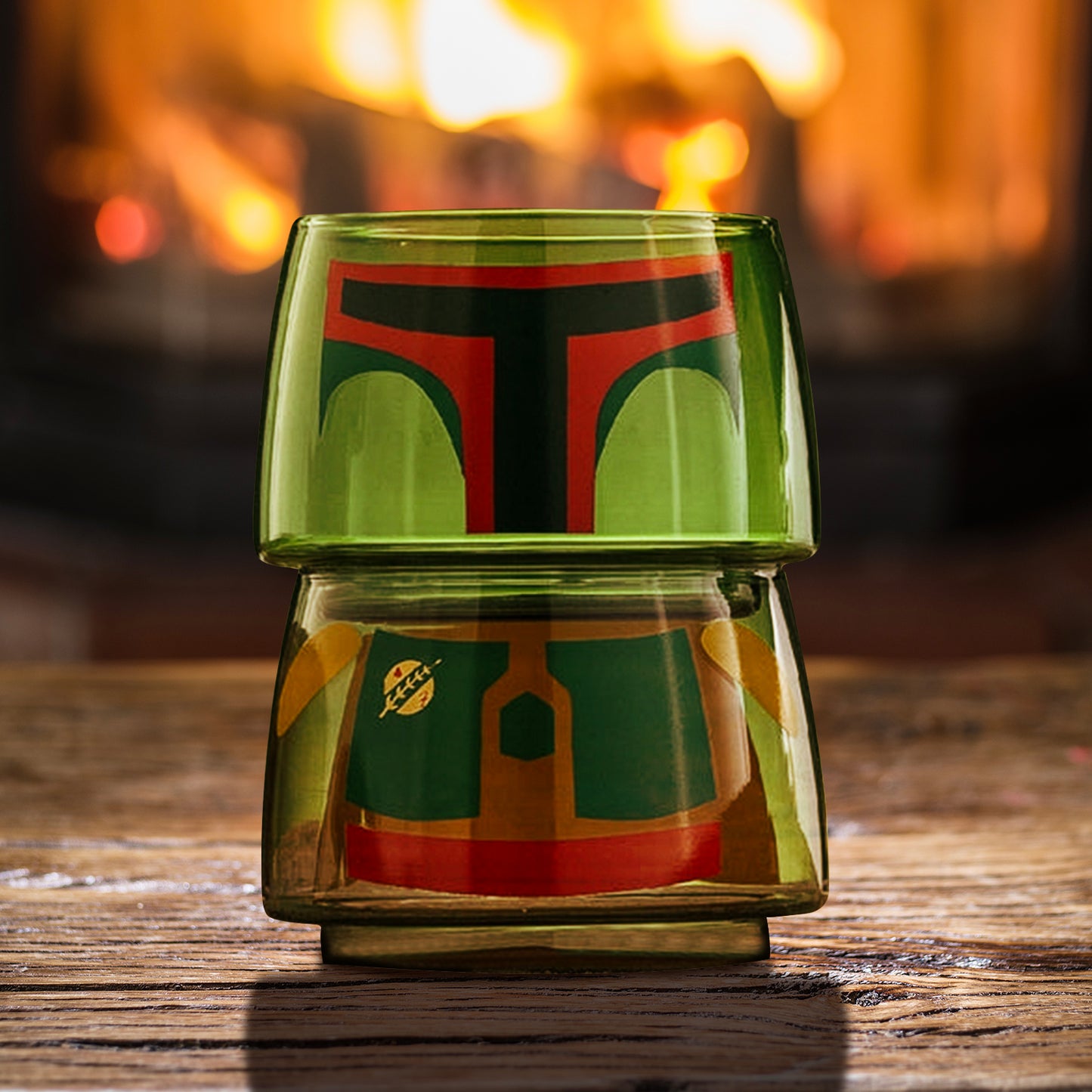 Two small drinking glasses stacked on each other on a wood table, with a fire in the distant background. The two glasses combined depict the character Boba Fett from the Star Wars movies. White text at the top says "Star Wars."