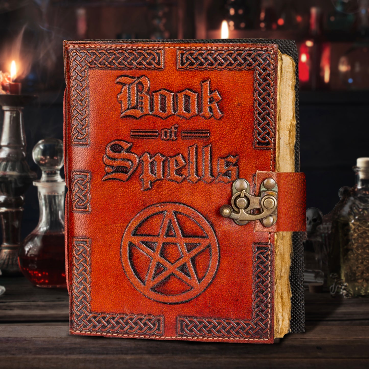 A brown leather book on a wooden table. Embossed text on the front cover says "book of spells," with an embossed pentagram symbol beneath it. On the right edge is a metal clasp to keep the book closed. In the background are bottles, jars, and other items found in an apothecary.