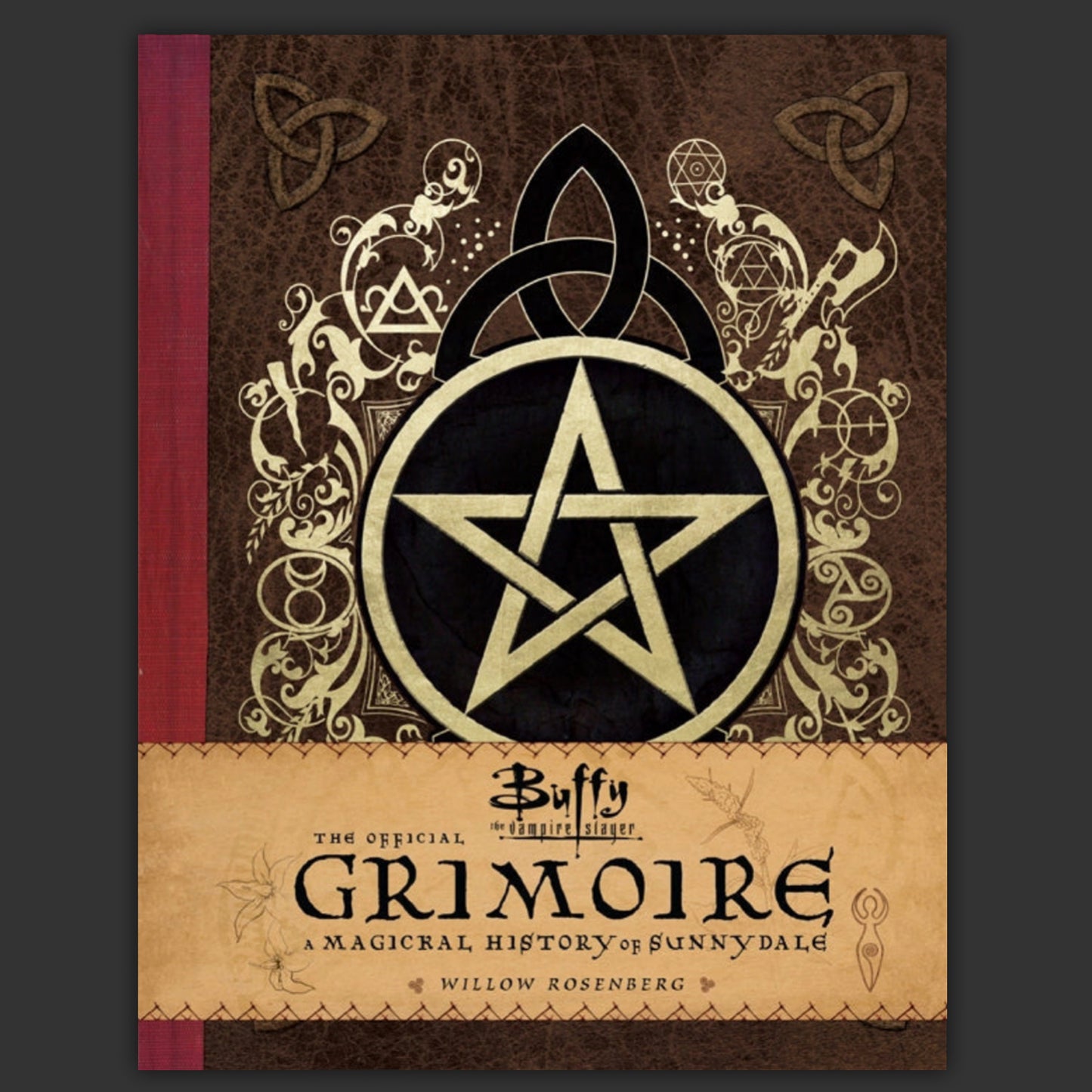 A hardcover book with a gold and black pentagram on the front cover. A brown band across the bottom says "Buffy the Vampire Slayer: The Official Grimoire."
