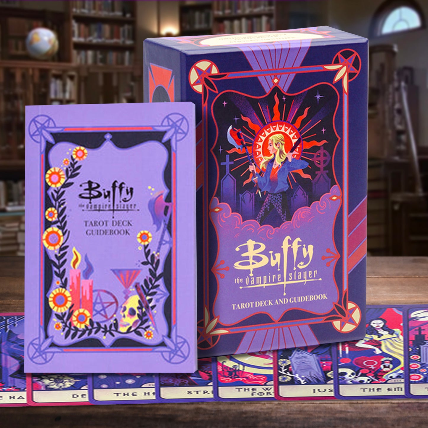 Buffy the Vampire Slayer tarot deck and guidebook set displayed on a wooden table, with the purple box, guidebook, and several illustrated cards visible in a softly blurred library background.
