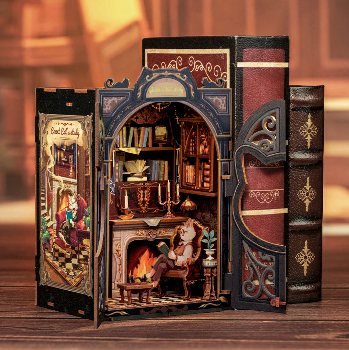 A paper book nook shelf decoration on a wooden table, next to a pair of hardcover books. The front of the book nook has ornate green doors, with a cat's head shaped cut out in the center. Inside is a miniature library, with a cat sitting on a plush chair, reading a book.