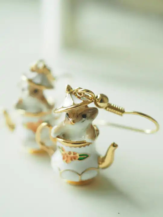 Load image into Gallery viewer, Close up view of two earrings against a white background. The earrings are shaped like an old-fashioned teapot, with a red flower in the center and gold accenting. The teapot&amp;#39;s lid is ajar, with a tiny chipmunk peeking out. Behind the earrings is a white and gold jewelry stand.
