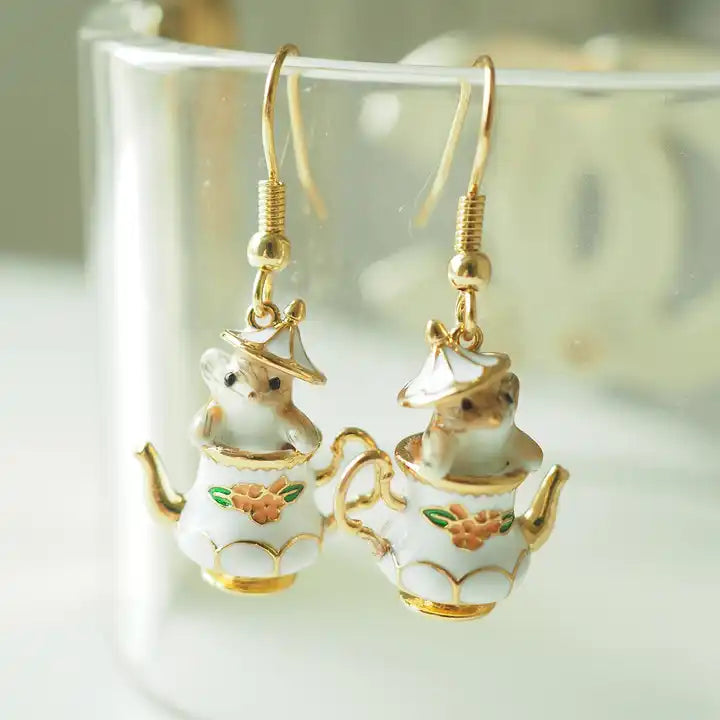 Load image into Gallery viewer, Close up view of two earrings hanging from the end of a round glass bowl. The earrings are shaped like an old-fashioned teapot, with a red flower in the center and gold accenting. The teapot&amp;#39;s lid is ajar, with a tiny chipmunk peeking out.
