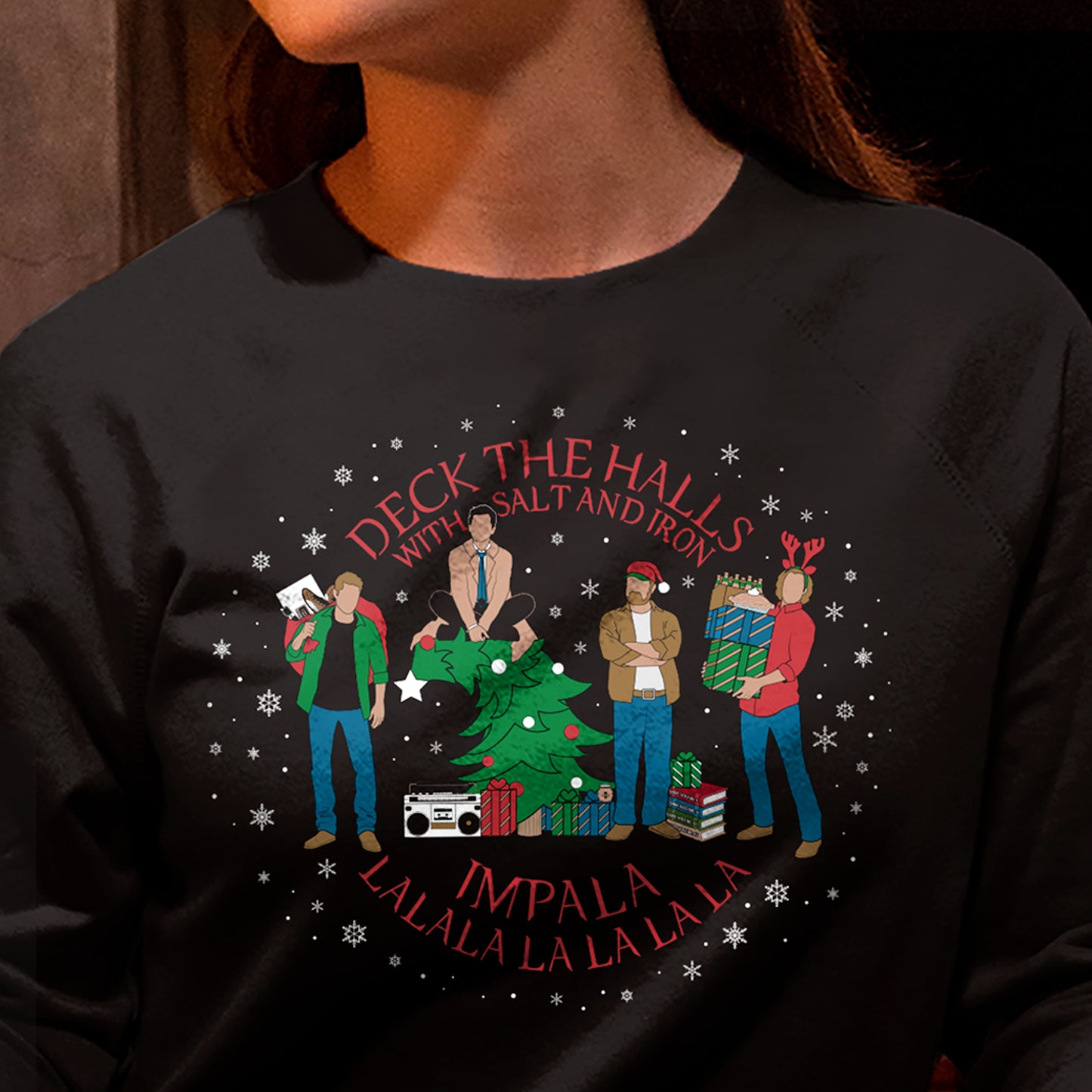 A model in a black sweatshirt, with a Supernatural themed holiday design on the front. Red text says "deck the halls with salt and iron. Impala lalala la la lala."