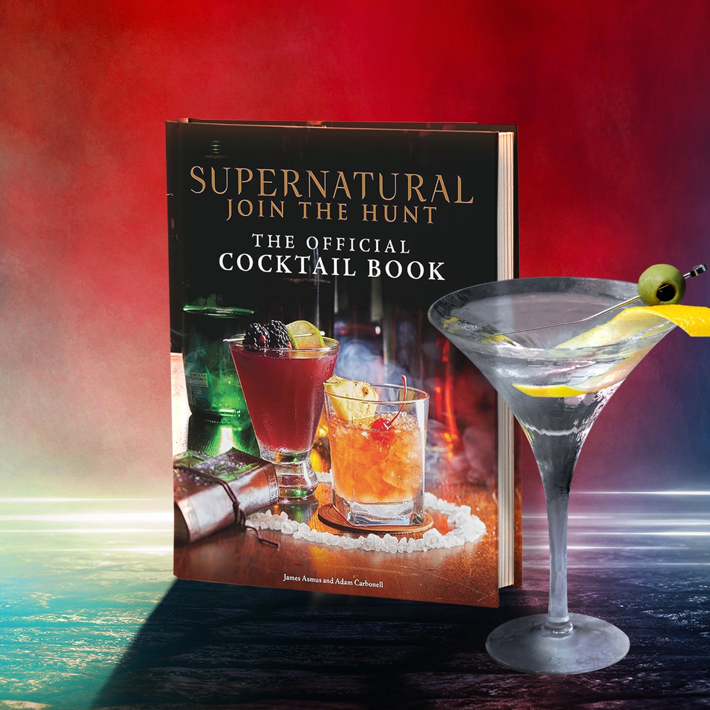 A book cover depicting various cocktails on a tabletop, sitting in a circle of salt crystals, against a red and green backdrop. Next to the book is a martini glass with an olive and lemon peel on the rim. At the top is gold text reading "Supernatural, Join the hunt." Below that in white text is "The official Cocktail Book."