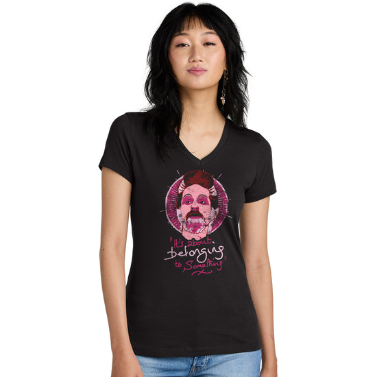 A woman in a black v-neck t-shirt that reads "It's about belonging to something" in white and pink cursive handwriting. Above the wods is an illustration of Con in a stylized beige, black, white, and hot pink palette, in front of a sun-like pink circle.