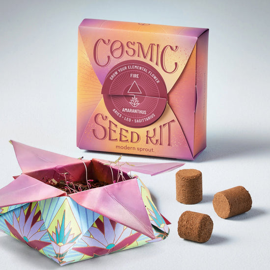 Two paper boxes against a white background. One box is covered in drawings of flowers, and is opened to show growing seeds inside. The second box is sealed, with red text that says "Cosmic seed kit. Grow your elemental flower. Amaranthus." Next to the opened box are three small cylinders made of soil