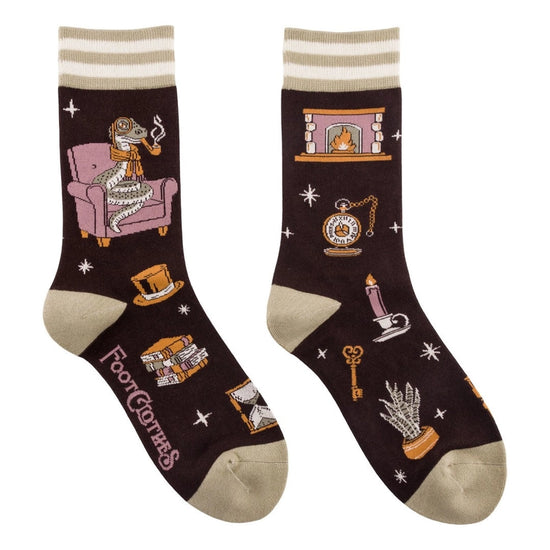 A pair of crew length black socks. The socks feature a pattern of candles, books, and other spooky items. On the side is a grey snake on a purple chair, smoking a pipe and wearing a brown scarf.