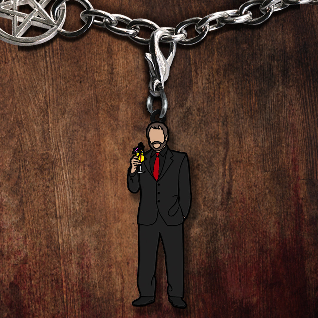 Keychain with a man in a suit and red tie holding a drink, on a wooden surface.