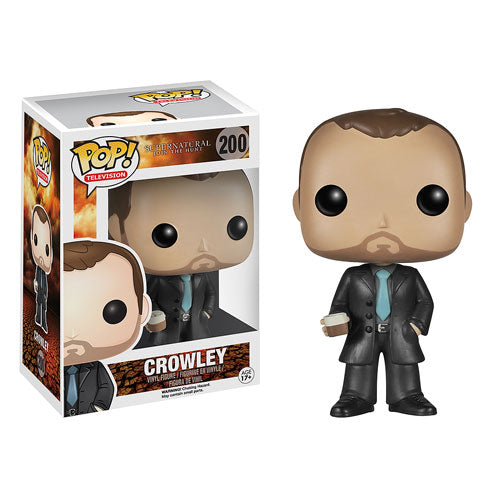 A vinyl Funko Pop figure of the character Crowley from the TV series "Supernatural." The figure is in a black suit with a light blue tie. In his right hand is a glass depicting single malt whiskey. Next to the figure is its box.
