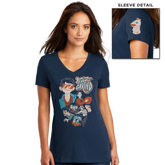 A picture of a female model in a navy blue v-neck t-shirt. The front of the tee is designed in a retro golden brown, cream, and light blue color scheme and reads "You've been Garth'd" above a series of depictions of Garth from Supernatural, including him wearing sunglasses, holding a cowboy hat, wearing a dentist mask, and doing an old-timey dance. One sleeve has a picture of the 'Mr. Fizzles' sock puppet.