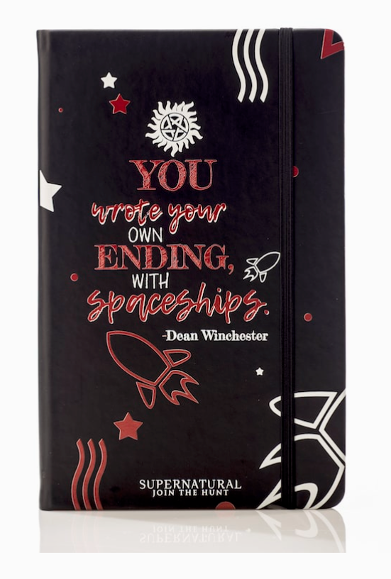A black journal against a white background. The front of the journal has red and white text saying "You write your own ending, with spaceships. Dean Winchester." At the top is a white anti-possession symbol. At the bottom is a red drawing of a rocket ship.