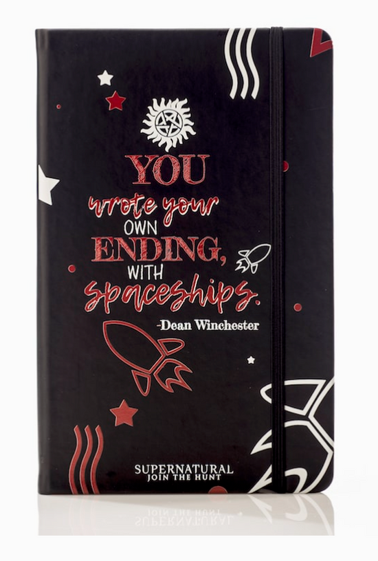 A black journal against a white background. The front of the journal has red and white text saying "You write your own ending, with spaceships. Dean Winchester." At the top is a white anti-possession symbol. At the bottom is a red drawing of a rocket ship.