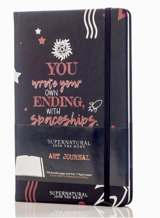 A black journal against a white background. The front of the journal has red and white text saying "You write your own ending, with spaceships. Dean Winchester." At the top is a white anti-possession symbol. At the bottom is a red drawing of a rocket ship.
