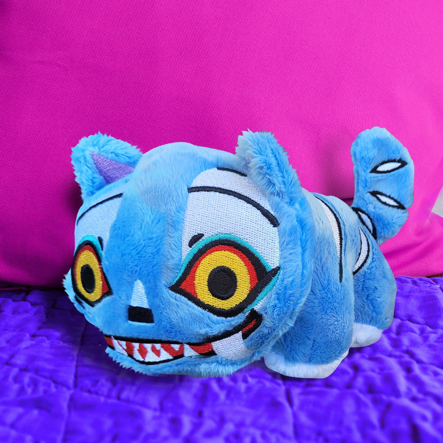 Blue plush toy with colorful face on a purple surface
