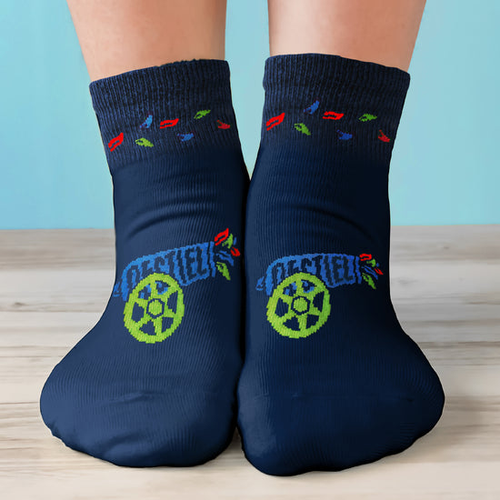 A model's feet wearing blue socks. The socks have a drawing of a blue cannon with a green white on the front. Rainbow colored feathers are shooting out of the cannon. A circle of rainbow feathers is printed at the ankle.