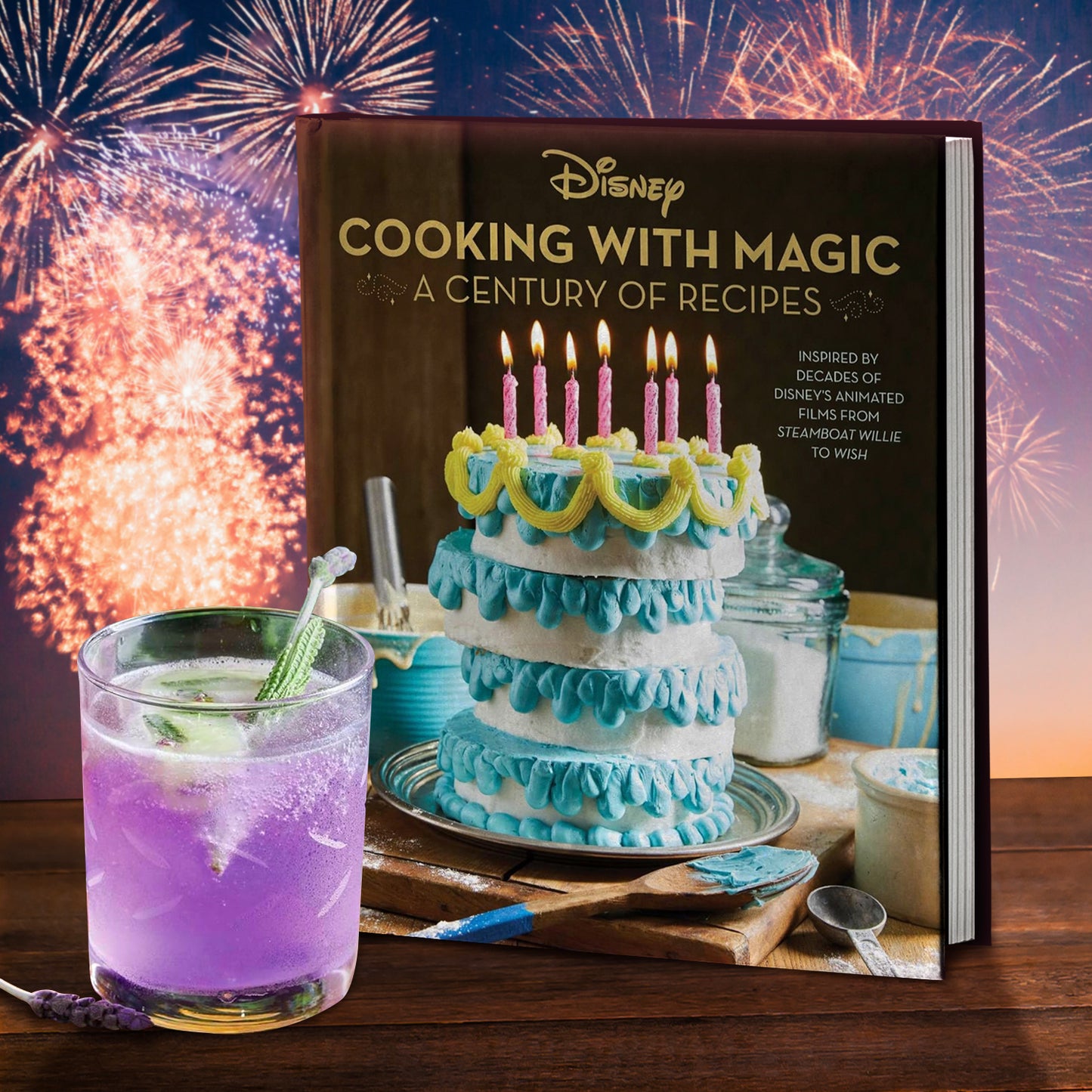 A brown cookbook cover with the Disney logo and the text: "COOKING WITH MAGIC: A CENTURY OF RECIPES" and "Inspired by decades of Disney's animated films from STEAMBOAT WILLIE to WISH". There is a blue, yellow, and white cake on the front with pink candles. The book is on a wooden table in front of fireworks, and there is a mixed drink sitting in front of it. 