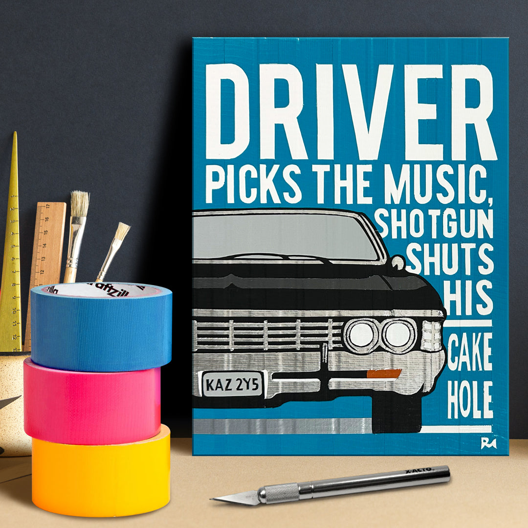 A blue poster against a dark gray wall. The poster depicts a black chevy impala, with white text saying "driver picks the music, shotgun shuts his cake hole." Next to the poster are rolls of colored duct tape and cutting tools.