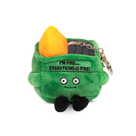 A female model holding a green, square plushie depicting a dumpster on fire. The plushie has large white eyes and small black legs. Black text at the top says "I'm fine. Everything is fine!" A metal chain is attached at the top.