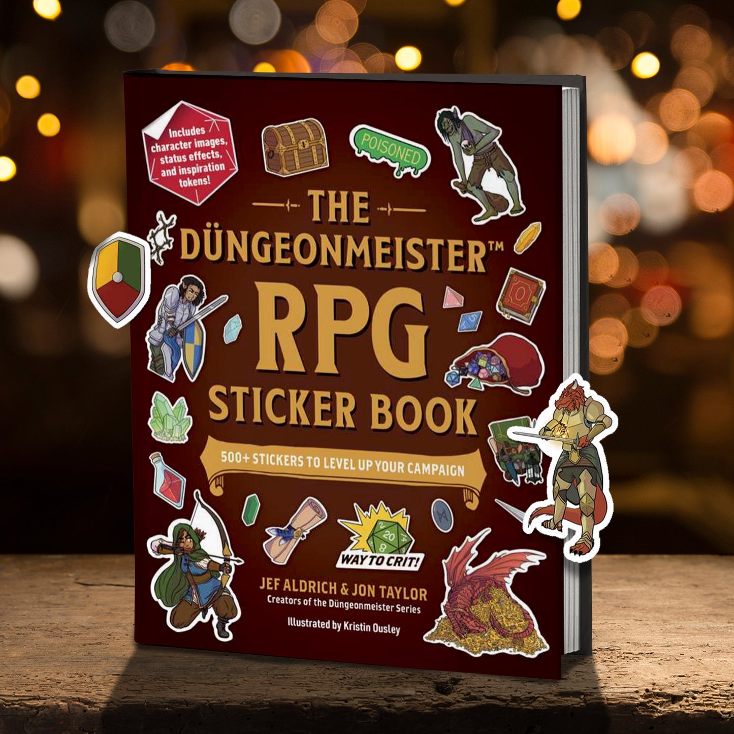 A brown book on a wooden ledge. The cover of the book has a collection of stickers scattered around it, each depicting a character or item that is typically found in fantasy role playing games. Light brown text says "The dungeonmeister RPG sticker book." In the background is a blurred field of lights