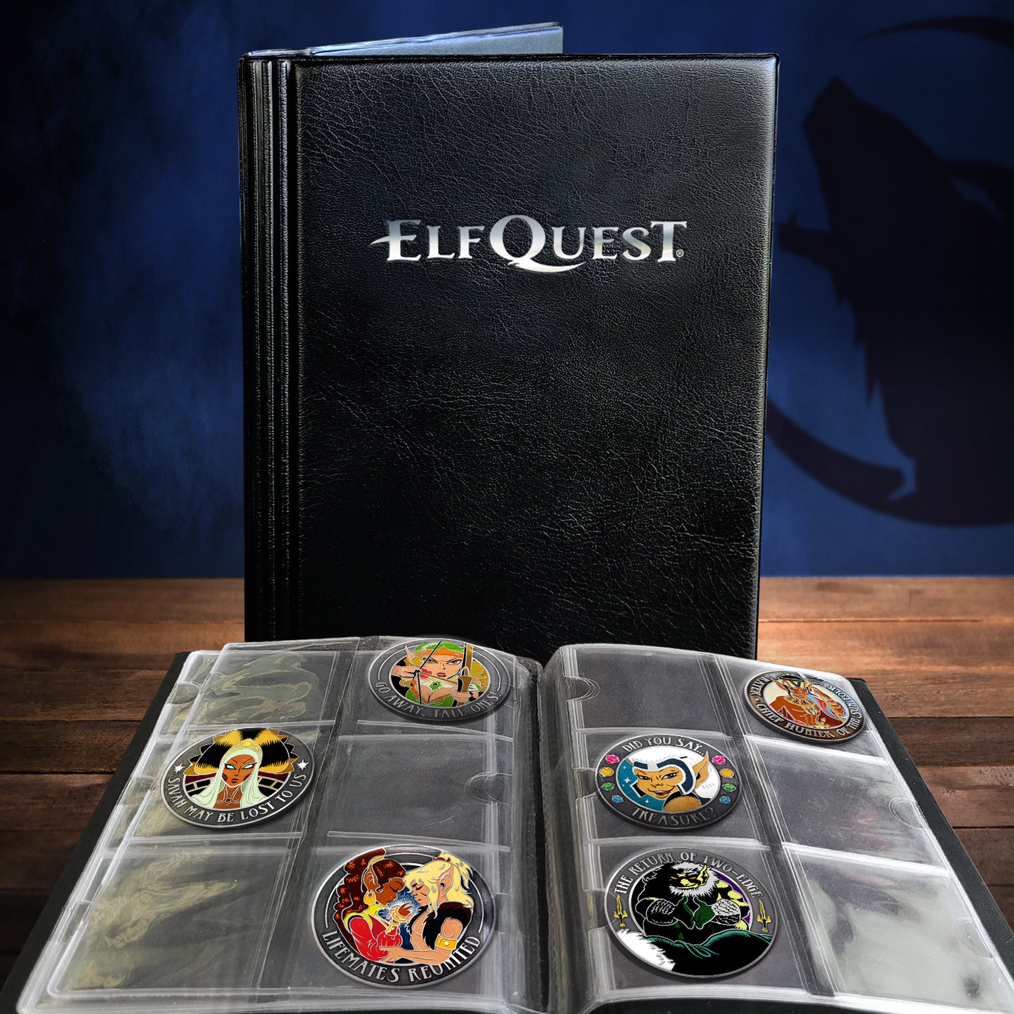 An open collectible coin album with multiple clear plastic coin slots, displaying several round fantasy-themed coins. A black faux-leather cover standing behind it is embossed with the brand name 'ELFQuest'.