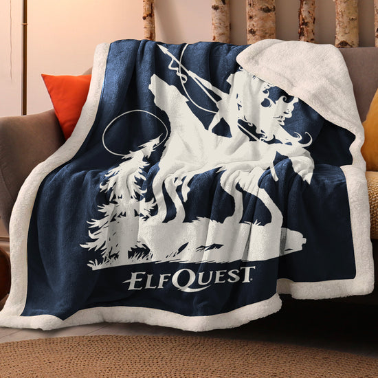 A blue and white sherpa blanket on a brown sofa. The blanket features a white silhouette drawing of the character Nightfall, astride her wolf companion Spar. Nightfall is holding a spear. Behind her is a tree, with two moons in the sky. Underneath them is white text saying "ElfQuest." Next to the blanket are red and yellow pillows on the sofa. Behind the sofa are narrow tree trunks.