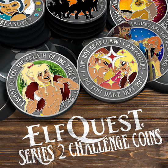 A pile of grey challenge coins on a wooden table. The front coin shows two ElfQuest characters glaring at each other. Behind that, a coin shows Cutter and his family. The back coin shows Two-Edge forging a knife. A back left coin shows Skywise and a coin beside that shows a group of wolfriders. The front left coin shows Cutter baring his chest.