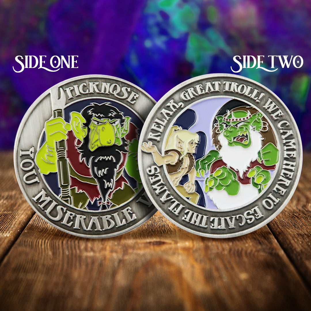 Front and back images of a brass challenge coin, on a wood table. The front of the coin depicts the ElfQuest character Picknose, with raised text saying "picknose, you miserable worm" around the edge. The back depicts a green troll, with raised text saying "relax you great troll! We came here to escape the flames." Behind the coin is an inky blue and purple background.
