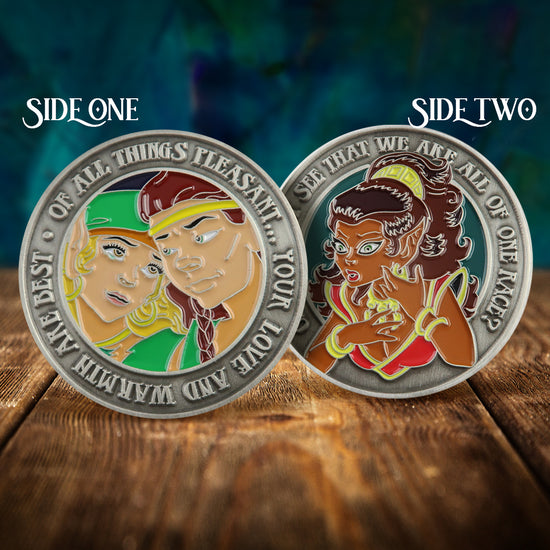 Front and back images of a brass challenge coin, on a wood table. The front depicts two ElfQuest characters, one a female with blonde hair in a green outfit, the other a male with brown hair and a yellow headband. Raised text around the edge reads "of all things pleasant, your love and warmth are best." The back depicts a dark skinned elf in a red outfit. Raised text aroiund the edge read "can you not see that we are all of one race?"