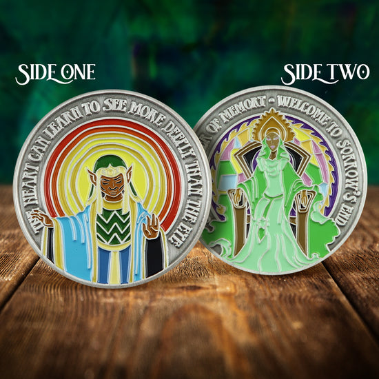 Front and back images of a brass challenge coin, on a wood table. The front depicts an elf in blue robes, with red and yellow waves radiating outward. Raised text around the edge reads "the heart can learn to see more deeply than the eye." The back of the coin shows an elf queen in green robes. Raised text around the egde reads "Savah, mother of memort, welcome to sorrow's end."
