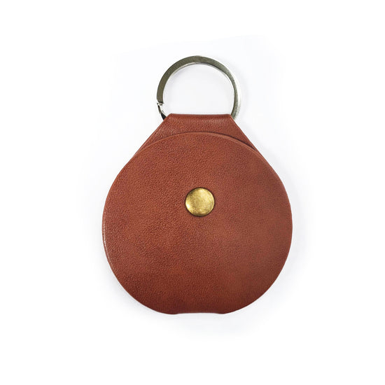 Load image into Gallery viewer, A round, leathery coin holder with a key ring at the top. In the center is a brass button that fastens the coin holder.
