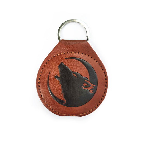 A round, leathery coin holder with a key ring at the top. In the center is a black embossed image of a howling wolf inside a crescent moon.