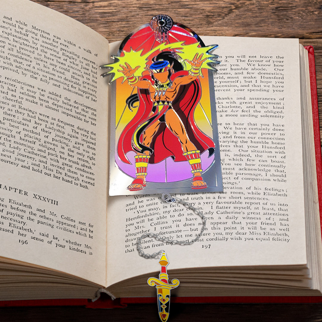 A metal bookmark between the pages of a hardcover book. The bookmark depicts the character Rayek from the ElfQuest series.