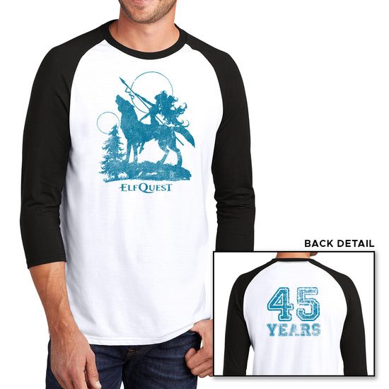 Two images of a male model wearing a white long sleeve T-shirt with black sleeves. The larger image has a blue image of an elf riding on the back of a large howling wolf, next to a small tree. The elf is holding a spear, and pointing it toward the sky. Under the wolf is text saying "ELFQUEST." The smaller image shows the back of the shirt, with "45 Years" printed in large blue text.