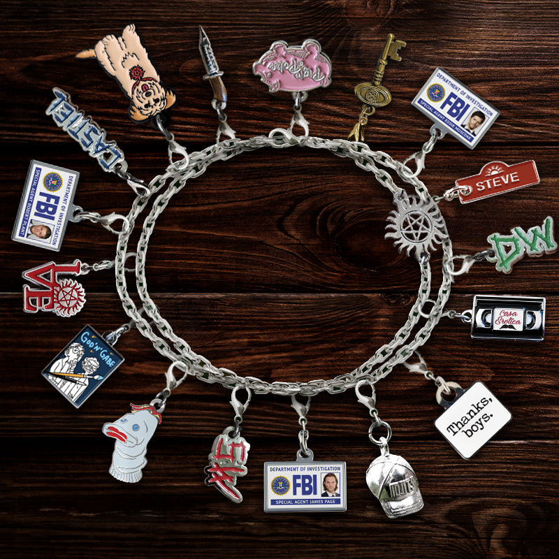 A silver charm bracelet with an anti-possession symbol in the chain. Various SPN-themed charms are attached to the bracelet in a circle. Beneath the charms is a dark brown wood table.