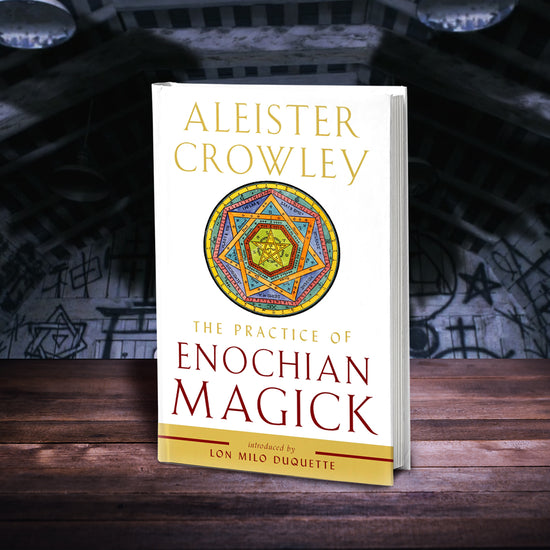 A white book on a wood table, set against a wall covered in magical symbols. At the top of the book in yellow text is the author's name, Aleister Crowley. Under the name is a muilti-colored Enochian symbol, consisting of a six point star set within concentric circles. Under the symbol in yellow text is the title "The practice of Enochian Magick." At the bottom of the cover is a yellow band, with red text reading "introduced by Lon Milo Duquette."