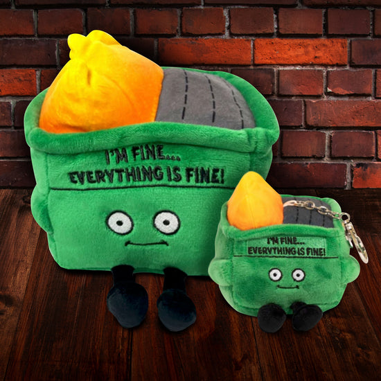 Two green, square plushies, both depicting dumpsters on fire. One is larger, and the smaller one has a metal keychain attached to the top. Both are on a wooden floor, against a brick wall. Both have black text on the front that says "I'm fine. Everything is fine!," with large white eyes and small black legs underneath.