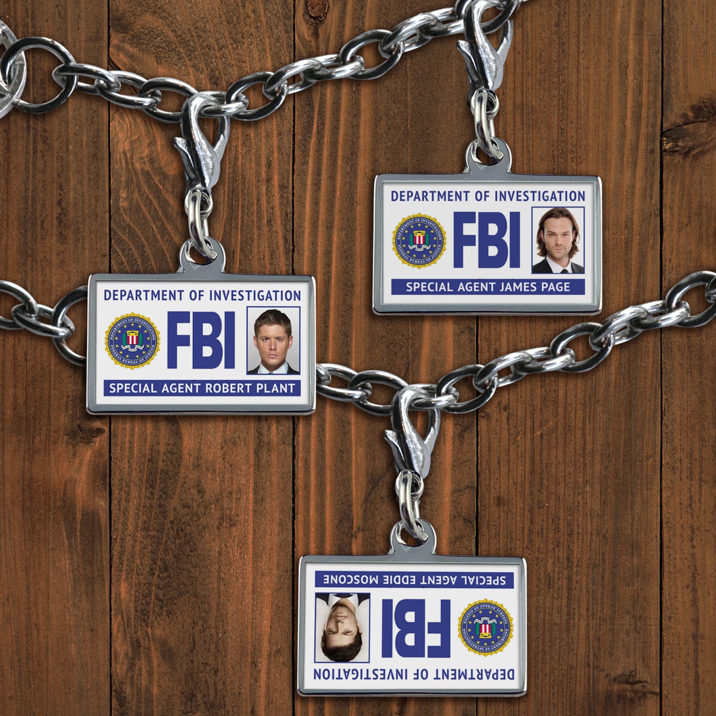 3 silver charms clipped onto a linked bracelet. Each of the charms is in the shape of a simple "FBI badge". They read "Department of Investigation: FBI" beside an FBI seal. One charm shows a picture of Dean Winchester, one shows Sam Winchester, and one (intentionally upside down) charm shows Castiel. 