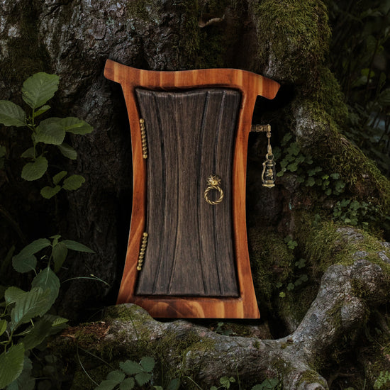 A miniature, curvy wooden door and frame, against a dark and mossy tree. The door is a dark gray color, with brass hinges and a round doorknob on the sides. Sticking out from the frame is a tiny brass post, with a miniature lantern hanging from it.
