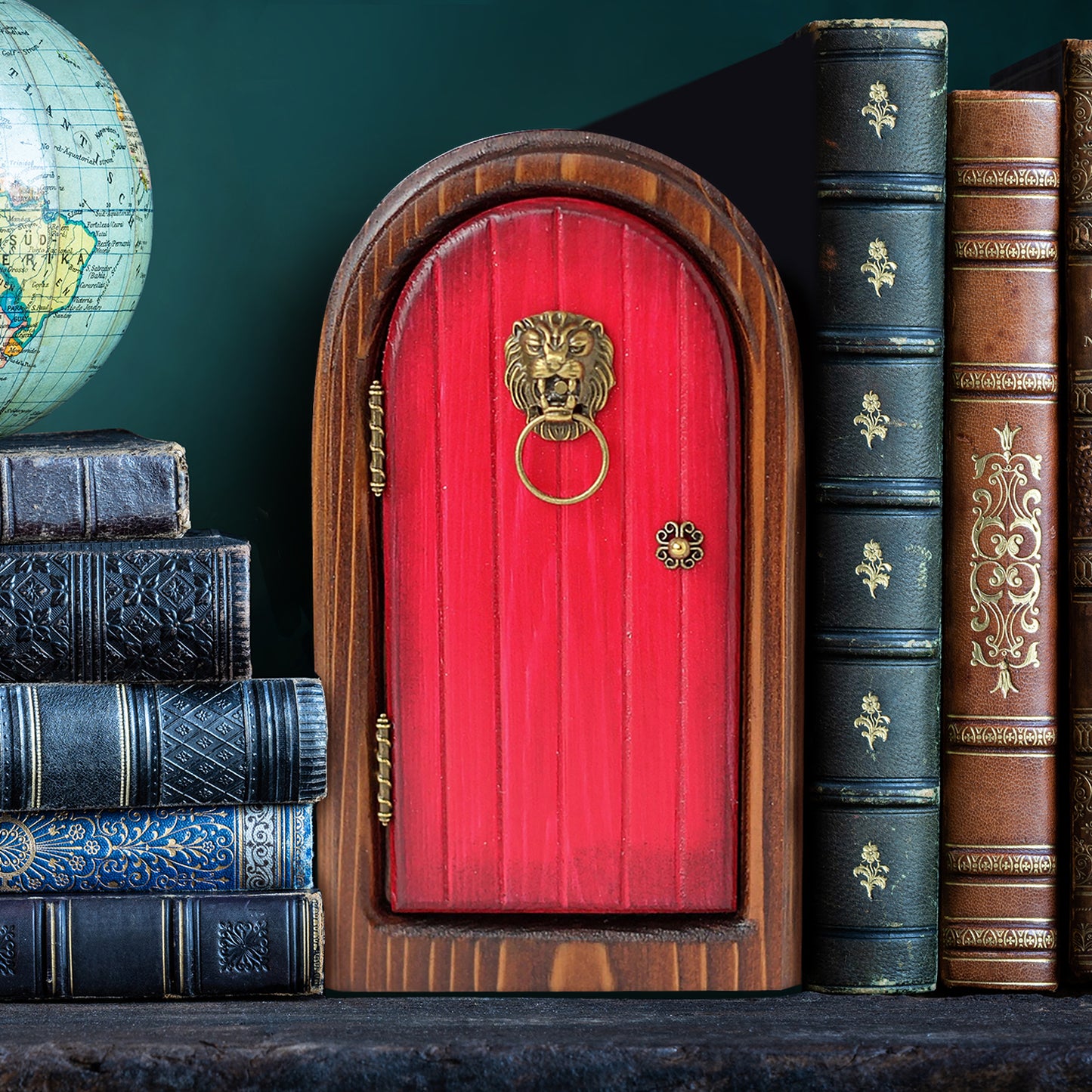 An arched wooden doorframe with a red door, sitting between leather-bound books. At the sides of the door are brass hinges. A brass doorknob sits at the right side, and a lion-head shaped knocker with a hood is at the top of the door.