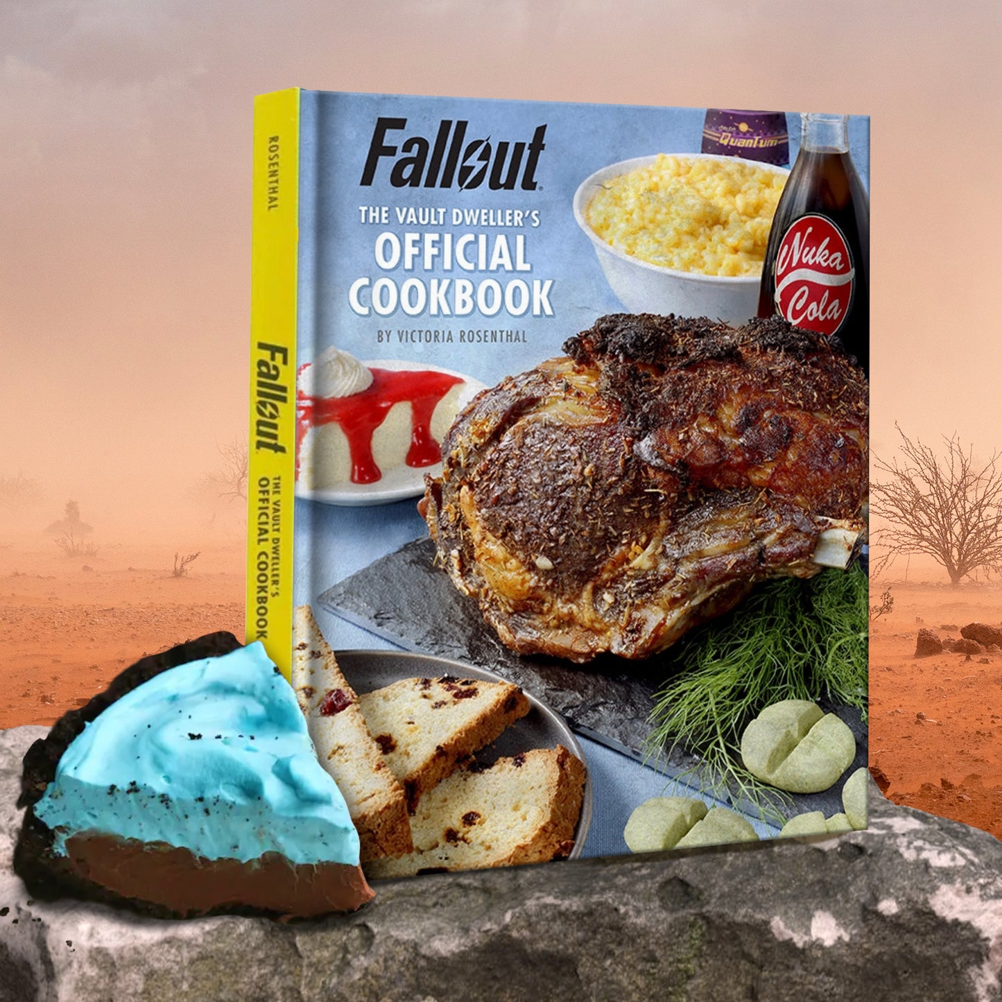 A hardcover cookbook on a rock ledge, in the middle of a red desert. Across the cover are various recipes from the book, including a roast meat dish, bread, and cheesecake. At the top left corner is black and white text that says "Fallout. The Vault Dweller's Official Cookbook." Next to the book is a slice of chocolate pie with a blue topping.