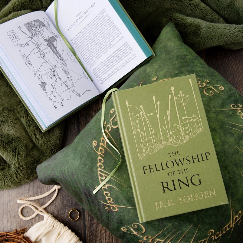Two green hardcover books on a green pillow. The front cover of one book depicts a minimalist drawing of a swamp in gold. Black text says "The Fellowship of the Rings." The second book is open to show a map depicting an area in Middle Earth.