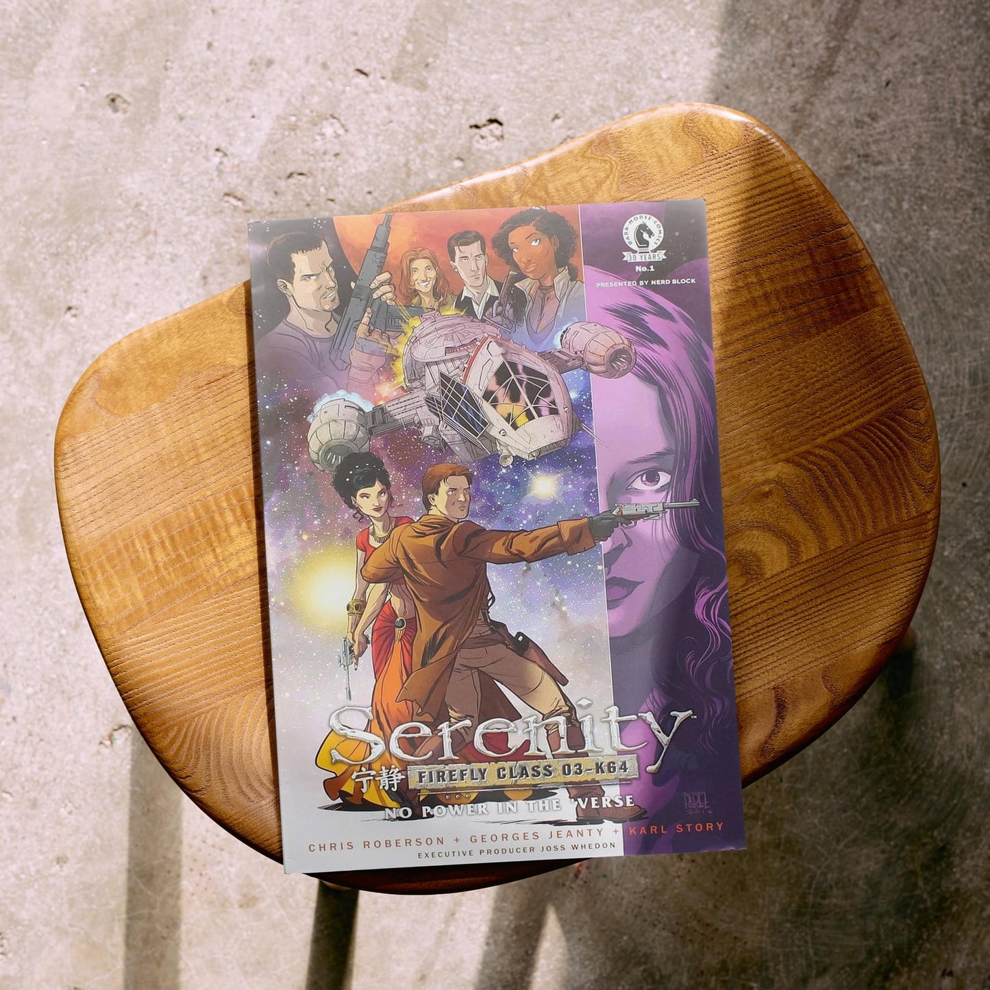 Comic book titled 'Serenity' on a wooden stool with a concrete floor background
