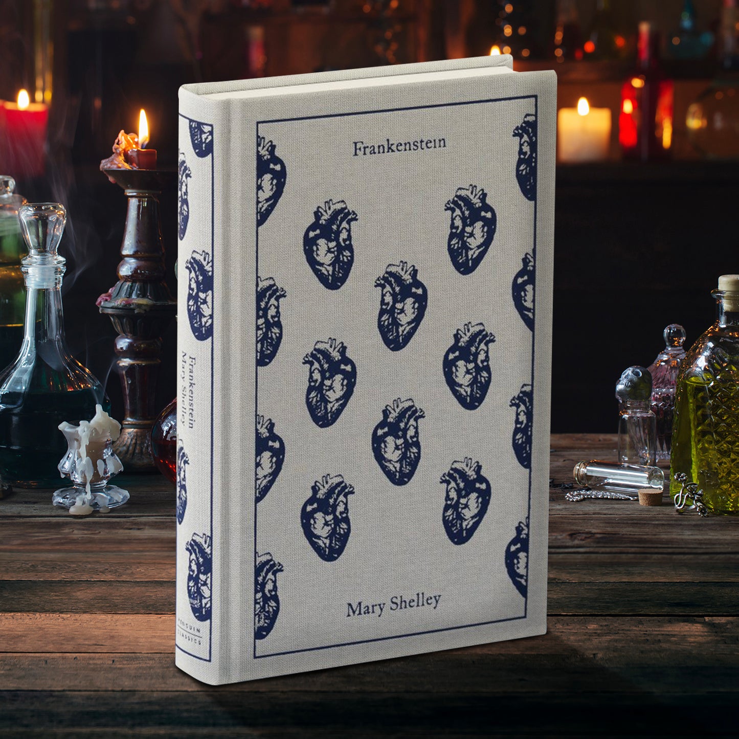 A clothbound hardcover copy of Mary Shelley's FRANKENSTEIN. It's a light grey cloth covered with a pattern of navy blue hearts. The book is sitting on a rustic wooden table.