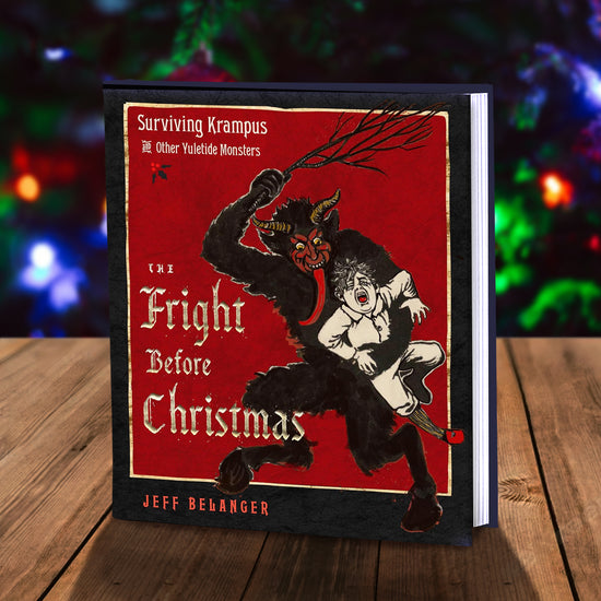 A red and black book on a wooden table, in front of Christmas lights. On the cover is a drawing of the European legend Krampus, a half-goat half-demon monster. Krampus is shown carrying a small child, with a broken tree branch held above his head, ready to strike the child. The book title “The Fright Before Christmas” is in yellow text.